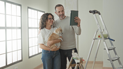 Man and woman, middle aged couple, smile as woman holds small dog and man's hand holds tablet to take a selfie in building  home renovation joy. © Krakenimages.com