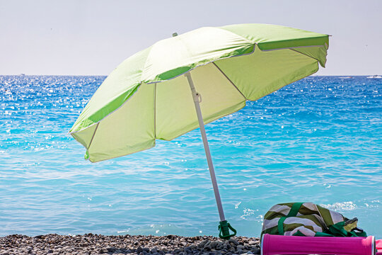 A lime-green beach umbrella on a pebble beach against the backdrop of the sea on a hot day. Seaside vacation. School holidays.
