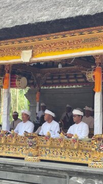 Three Indonesian men in traditional attire play musical instruments in a decorated pavilion. The scene captures cultural performance and community spirit.