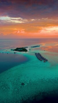 A beautiful paradise island in the Maldives with water bungalows over the turquoise ocean with shining coral reefs during sunset
