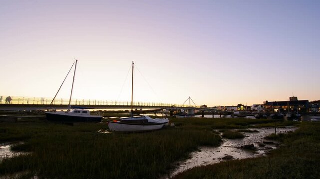 Sunset over a coastal town with boats in a river, transitioning from golden hour to darkness as town buildings and street lights gradually illuminate x2 speed