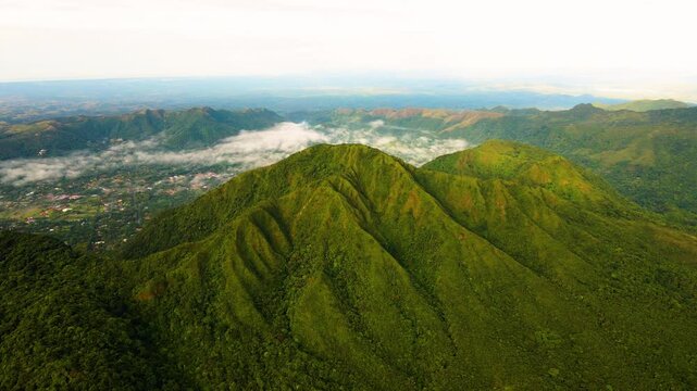 Cerro el Gaital, Panama. Lush green mountains roll toward a hazy horizon. Soft clouds float low among the valleys. Distant peaks fade into gentle blue. Sunlight bathes the hills in warm tones. Drone.