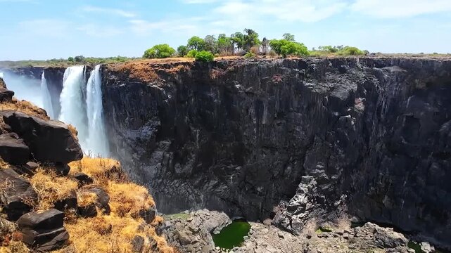 A dry season view of Victoria Falls reveals steep exposed canyon walls and the narrow Zambezi River below, with a remaining waterfall at the gorge edge.