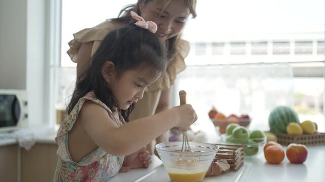 Daughter joyfully whisking egg mixture with mother nearby