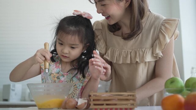 Mother supervising daughter whisking egg mixture in glass bowl