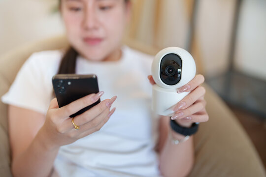 Asian woman configuring white smart home security camera with smartphone mobile app