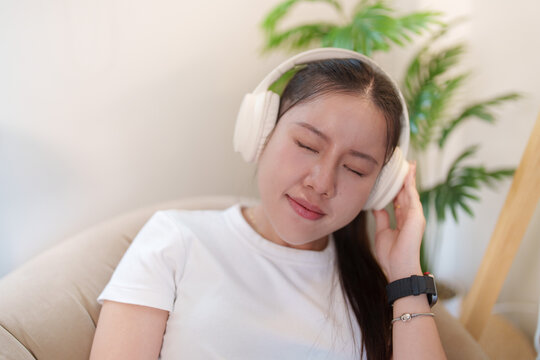 Asian woman wearing headphones relaxing with eyes closed for smart home audio concept