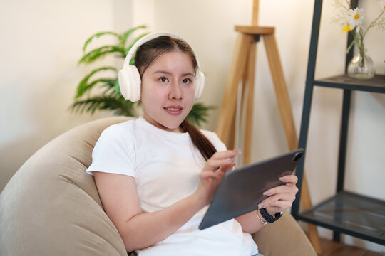 Asian woman using digital tablet with headphones for smart home device control