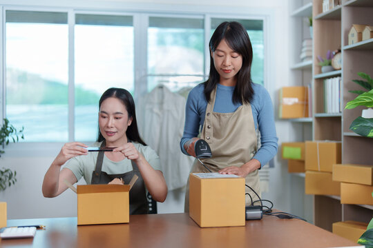 Asian female entrepreneurs scanning package and taking photo for small business online store
