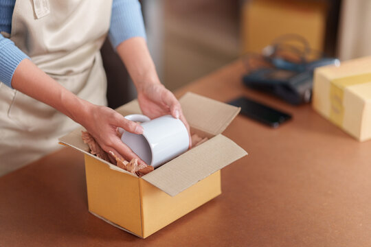 Small business owner packing ceramic mug into cardboard box for online order fulfillment