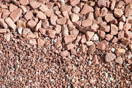 Red granite chippings background closeup with two kinds of crushed stone gravel, one large fraction and one small fraction sizes comparison for garden landscaping, horizontal top view flat lay copy.
