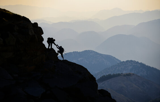Two Climbers Reaching for Each Other at Sunset, a Symbol of Success