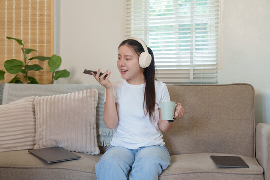Asian woman using smartphone voice assistant for smart home control in living room
