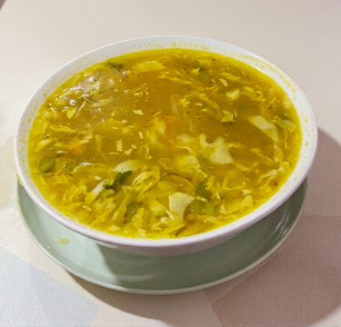 A bowl of traditional Indonesian chicken soup soto ayam with shredded chicken, cabbage, and savory yellow broth served in a bowl.