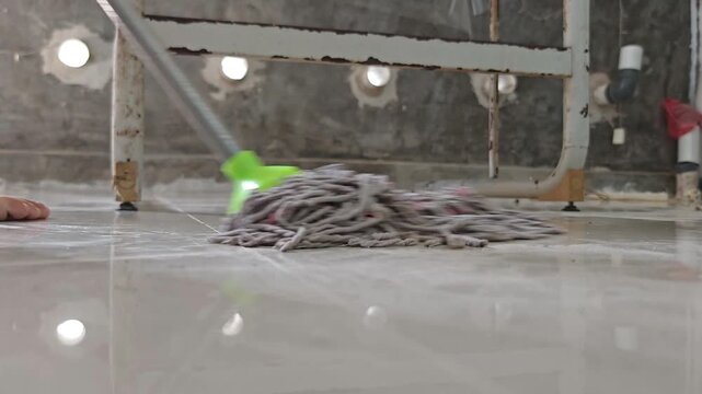 a person's bare foot standing on a wet, reflective tile floor while a string mop cleans the surface nearby.