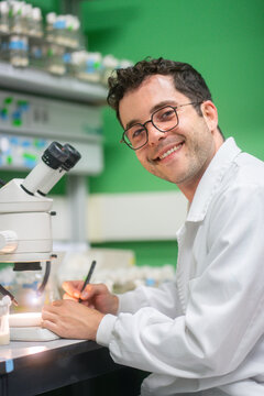 Male scientist writes notes beside a microscope
