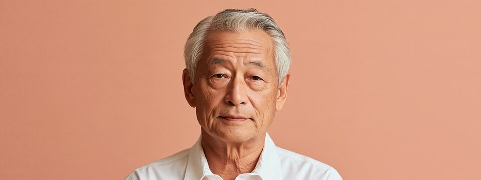 Portrait of a confident senior Asian man with grey hair against a plain bac