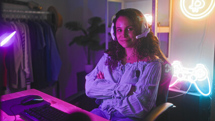 Woman gamer with headset sits at computer desk with arms crossed in studio under purple neon lights  confidence focus. © Krakenimages.com