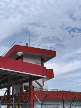 Fire station building at RHA Airport in Tanjung Balai Karimun, Indonesia, featuring a modern red structure with observation deck and secure perimeter under a partly cloudy sky.