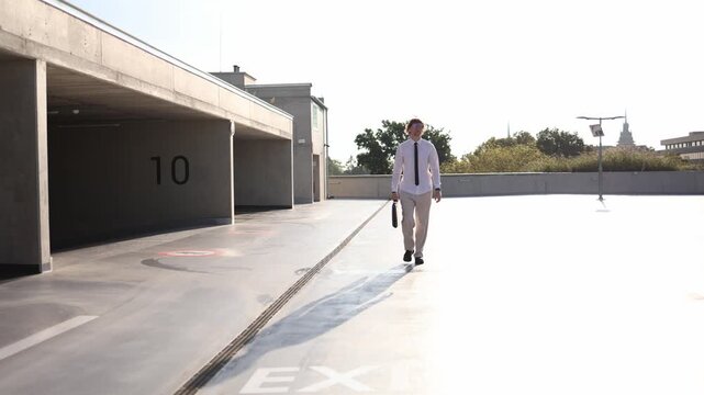 Young man rushes to his new job carrying a black briefcase while running across an outdoor parking lot in a white shirt and tie feeling excited and nervous about his first day at work