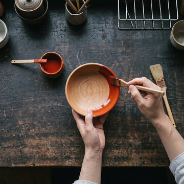 Hand brushing red urushi lacquer on wooden bowl Japanese lacquerware craft, flat lay with copy space at bottom