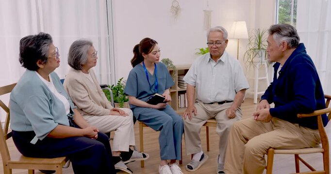 Senior Asian man explains health and rehabilitation concerns to Asian nurse and residents, using hand gestures during group consultation in assisted living community supporting wellness and recovery.