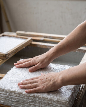 Hands holding washi papermaking frame with wet kozo fibre sheet Japanese paper craft, close-up with copy space at top