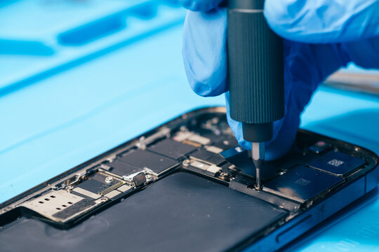 technician repairing internal micro-electronics component inside an opened smartphone on a blue mat as a concept for hardware maintenance service, right to repair information technology