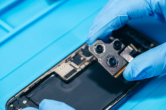 technician repairing internal micro-electronics component inside an opened smartphone on a blue mat as a concept for hardware maintenance service, right to repair information technology