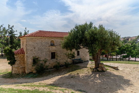 Stone chapel of Agios Pavlos beside an old olive tree and a bench with the red-roofed village behind, Nea Fokea, Kassandra, Chalkidiki, Greece