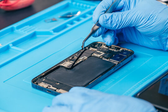 technician repairing internal micro-electronics component inside an opened smartphone on a blue mat as a concept for hardware maintenance service, right to repair information technology