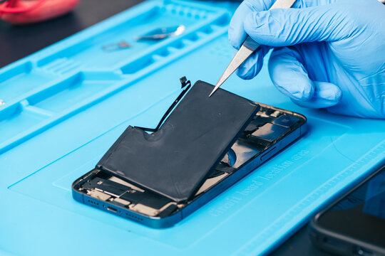 technician repairing internal micro-electronics component inside an opened smartphone on a blue mat as a concept for hardware maintenance service, right to repair information technology