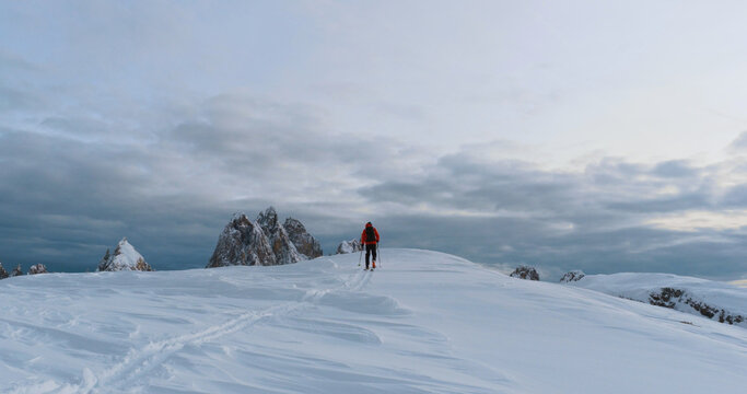 Ski mountaineer crossing a snowy ridge in the Dolomites with dramatic alpine peaks and blue sky in the background, capturing winter adventure and breathtaking mountain landscape.