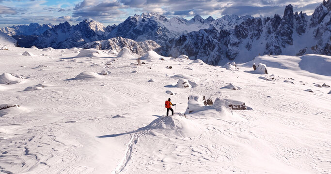 Ski mountaineer crossing a snowy ridge in the Dolomites with dramatic alpine peaks and blue sky in the background, capturing winter adventure and breathtaking mountain landscape.