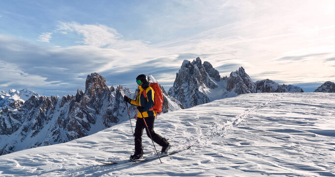 Ski mountaineer crossing a snowy ridge in the Dolomites with dramatic alpine peaks and blue sky in the background, capturing winter adventure and breathtaking mountain landscape.