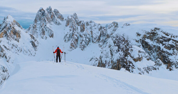 Ski mountaineer crossing a snowy ridge in the Dolomites with dramatic alpine peaks and blue sky in the background, capturing winter adventure and breathtaking mountain landscape.