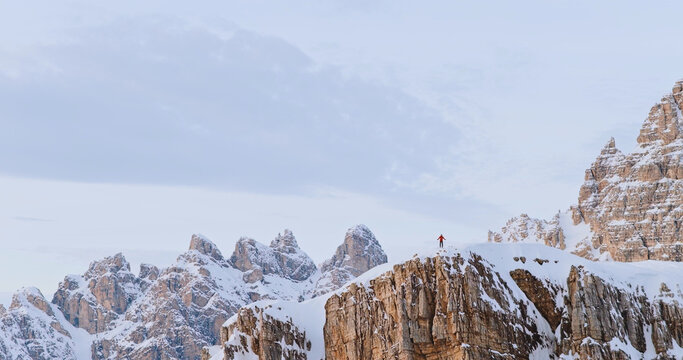Ski mountaineer crossing a snowy ridge in the Dolomites with dramatic alpine peaks and blue sky in the background, capturing winter adventure and breathtaking mountain landscape.
