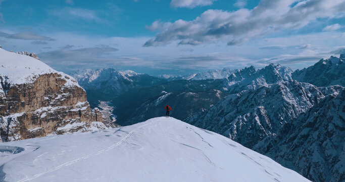 Ski mountaineer crossing a snowy ridge in the Dolomites with dramatic alpine peaks and blue sky in the background, capturing winter adventure and breathtaking mountain landscape.