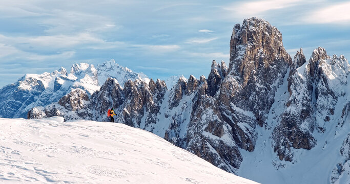 Ski mountaineer crossing a snowy ridge in the Dolomites with dramatic alpine peaks and blue sky in the background, capturing winter adventure and breathtaking mountain landscape.