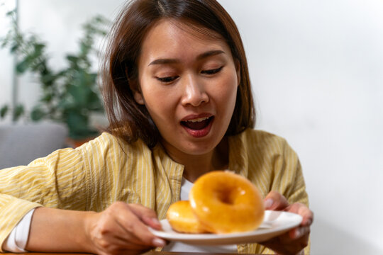 Woman holding up a plate of glazed doughnuts with mouth open