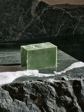 Green herbal soap bar on dark textured stone with white foam for spa and skincare product display