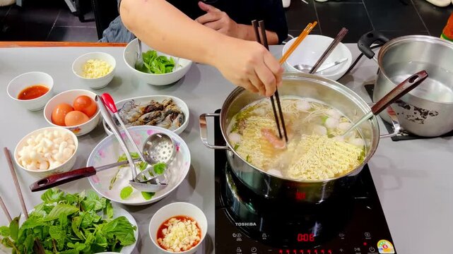 Hot pot noodle seafood vegetable broth meal hand table cooking scene with fresh ingredients, chopsticks, egg, mushroom, dipping sauce, shared Asian dining and warm communal soup gathering at home