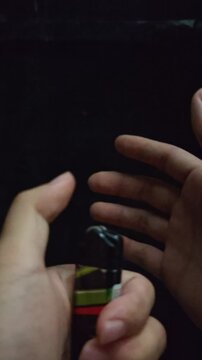 hands holding a portable lighter burning steadily in pitch black darkness. A bright yellow and blue flame illuminates the person's hands. Cinematic low light concept of fire, heat, survival, arson, an