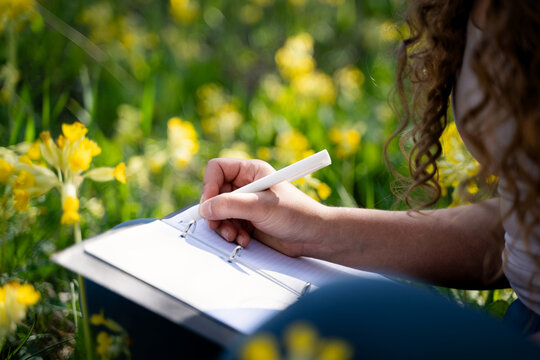 Close view of a woman taking notes in an open notebook while spending quiet time in a colorful spring meadow.
