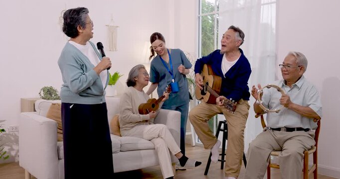 Asian senior residents sing and play guitar, ukulele and tambourine while female nurse joins music activity in assisted living center, encouraging social engagement, companionship and active aging.