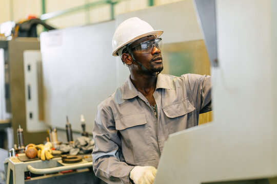 Black Engineer Operating CNC Machine in Factory Checking Industrial Manufacturing Process Control