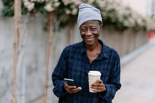 Smiling person holding coffee and phone on a blossom-lined urban walkway background for social media banner and lifestyle poster