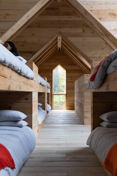 Natural wooden bunkhouse interior with gray linens and orange throws for cabin dormitory background and retreat design