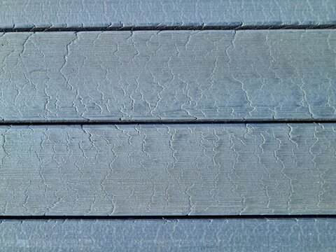 Macro view of painted grey wooden planks with fine cracks in the paint layer forming a weathered timber texture background.