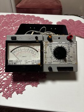 Vintage analog multimeter with dial and needle gauge on a lace tablecloth